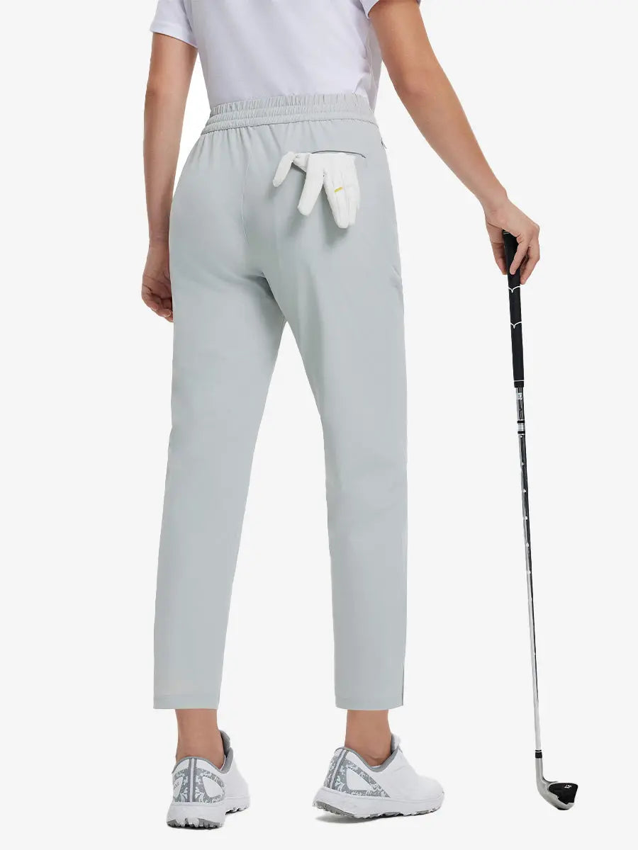 Back lower-body view holding a golf ball with glove in rear pocket wearing GLACIER GREY Women's 7/8 Ankle Golf Track Pants.
