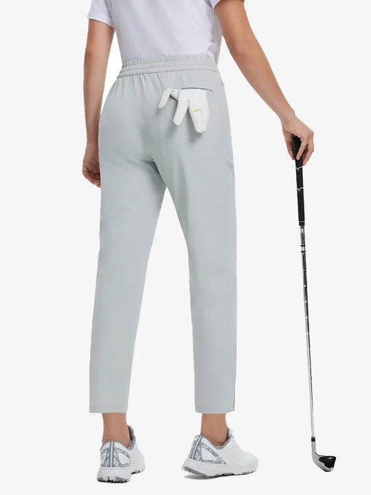 Back lower-body view holding a golf ball with glove in rear pocket wearing GLACIER GREY Women's 7/8 Ankle Golf Track Pants.