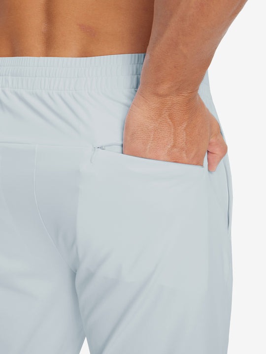 Back view of model with hand in pocket wearing lightweight traning track pants in misty grey.