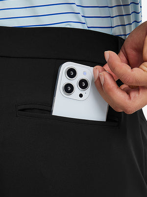 Close detail of hand placing phone into back pocket of lightweight moisture wicking dress pants in black.