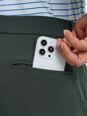 Close detail of hand placing phone into back pocket of lightweight moisture wicking dress pants in dark green.