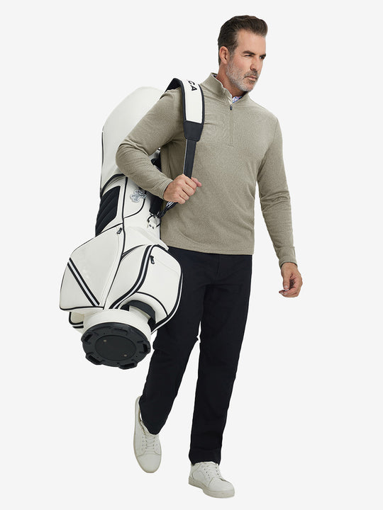 Model carrying golf bag on back, wearing casual fleece lined quarter zip pullover in dust beige, full-body.