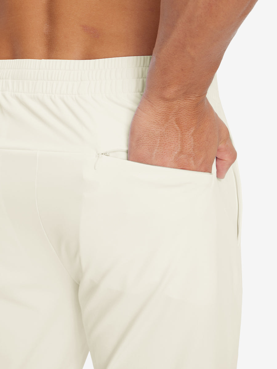 Back view of model with hand in pocket wearing lightweight traning track pants in cream.