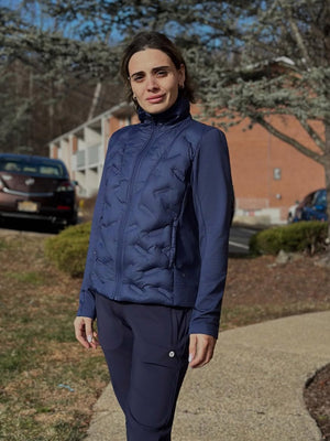 Model standing on a path with trees and houses, wearing navy women's lightweight fleece-lined puffer jacket.
